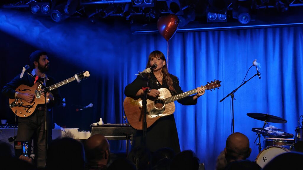 Kvinna med gitarr som sjunger i blått ljus.