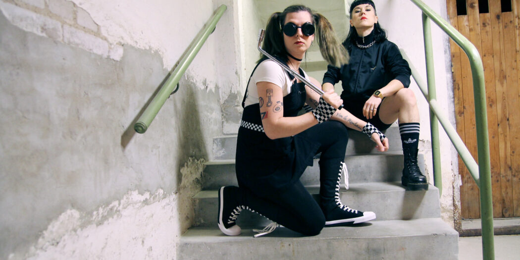 Lizzy och Emma i The Guilt sitter i en betongtrappa.