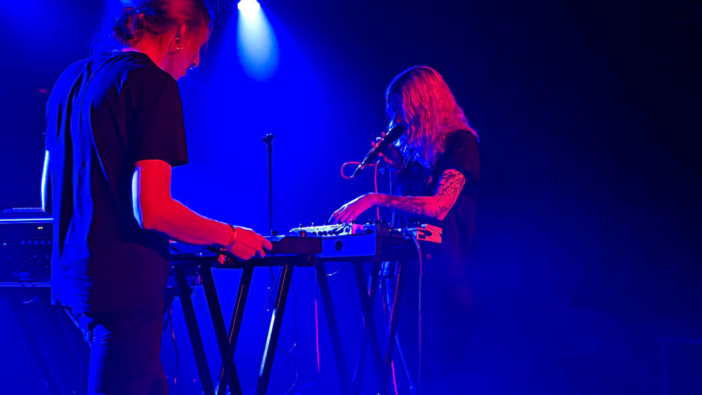 En kille och en tjej vid synthar i blått ljus.